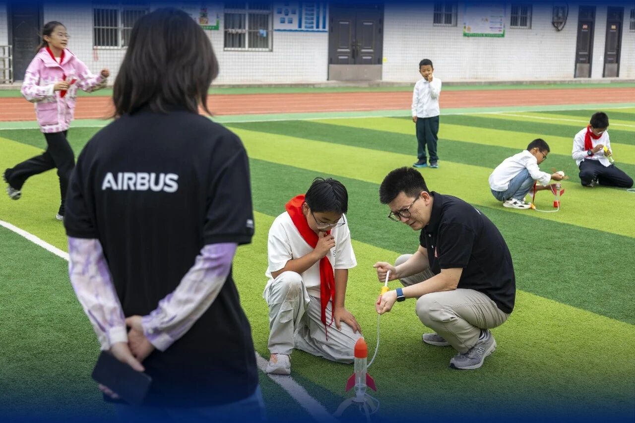 Students and adults inspect water-rocket setups on a school field.