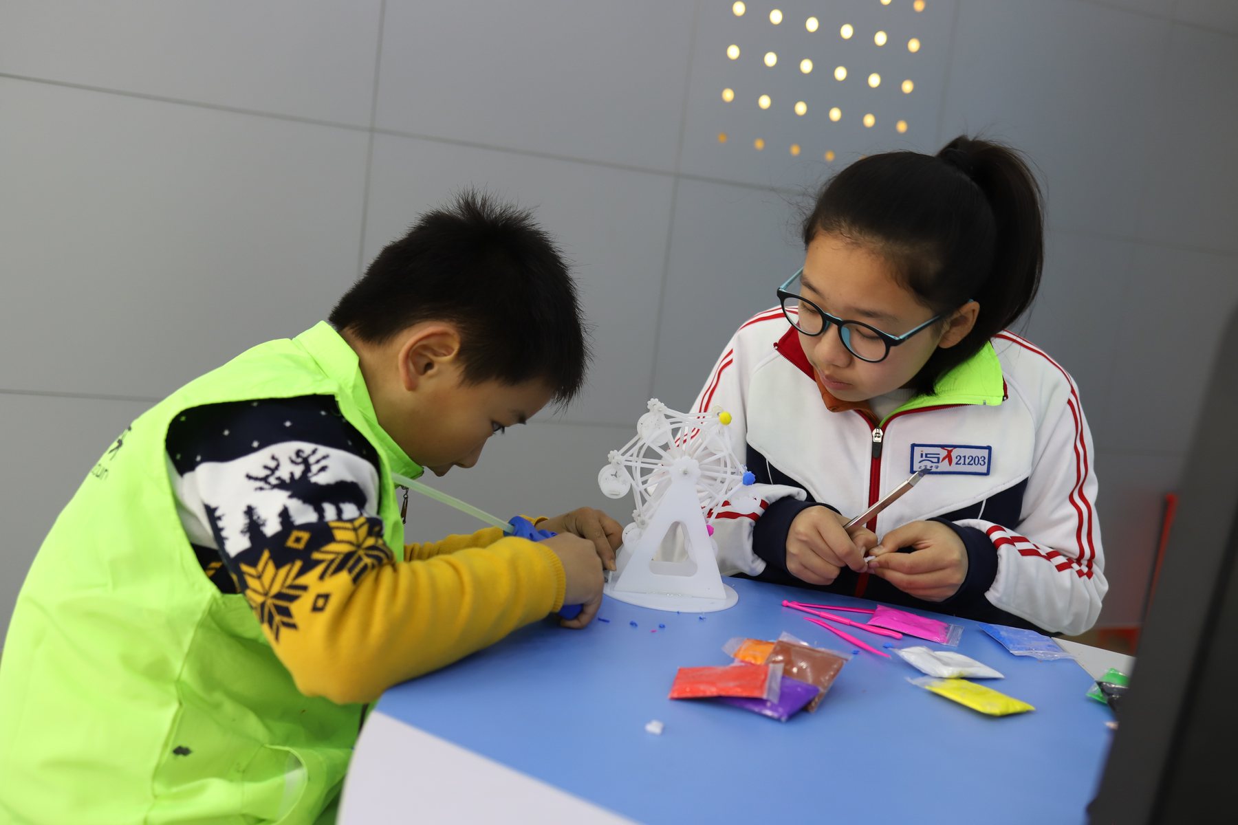 Two students assembling a small wheel-like model at a table.