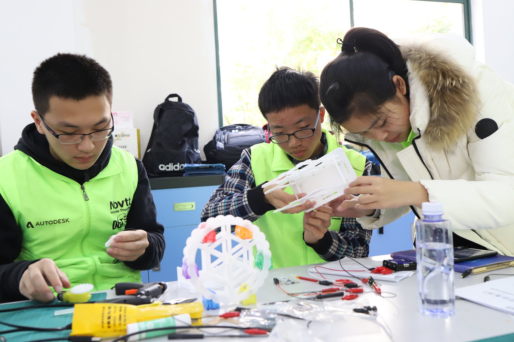 Two students and an adult examining a small constructed model at a worktable.