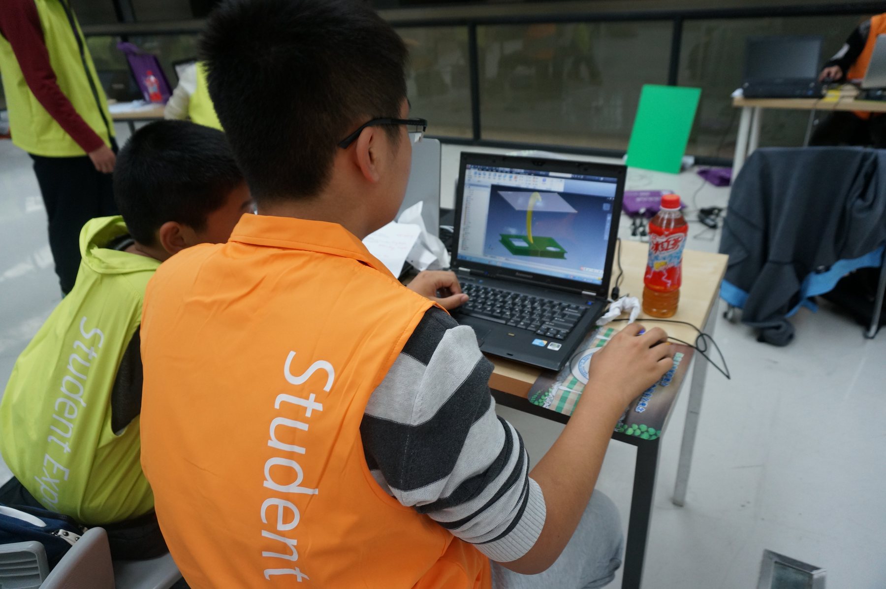 Two students working at a laptop displaying a three-dimensional design.